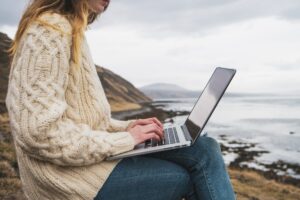 Iceland, woman using laptop at the coast